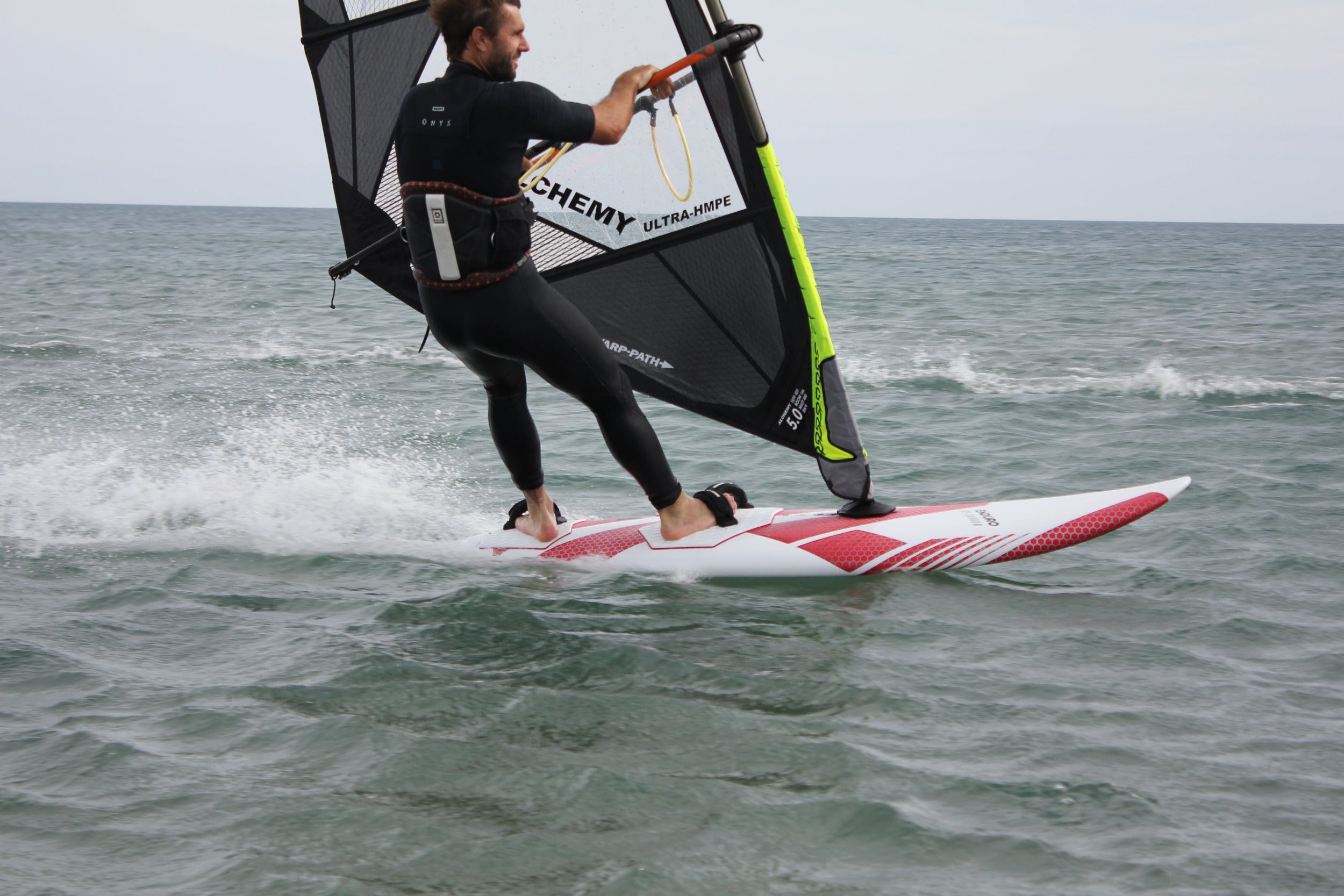 Person windsurfing on a body of water with a sail and board.